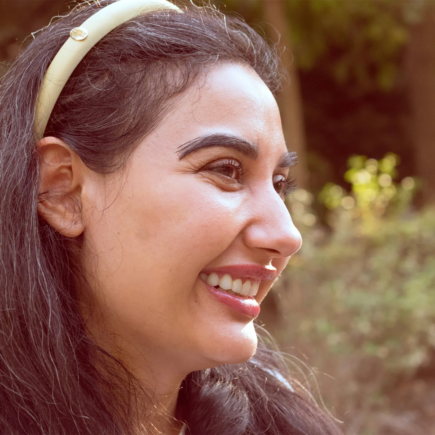 Mujer sonriendo al aire libre, con luz natural, mirando hacia un lado.